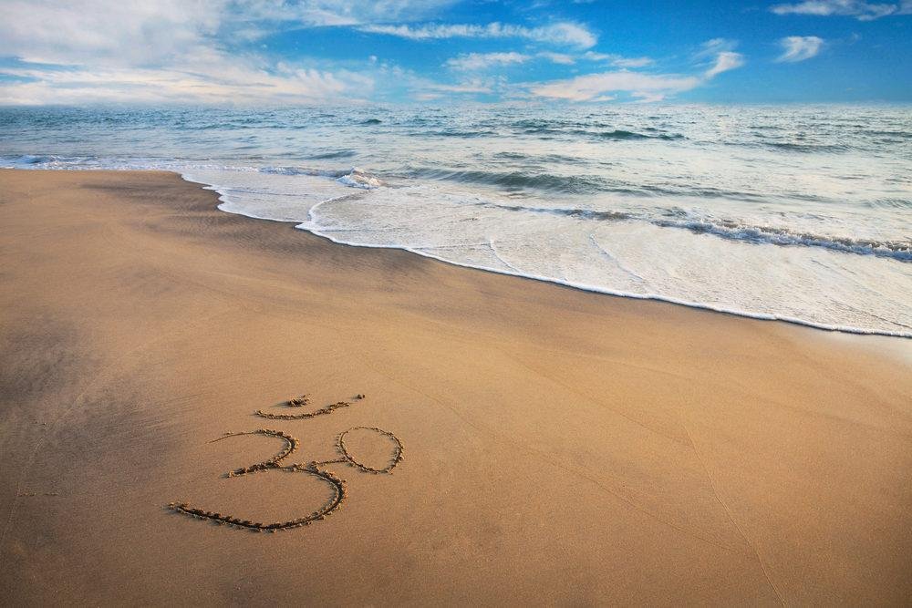 Aum symbol drawn in sand at a serene beach with ocean waves.