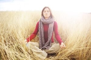 Woman meditating peacefully in a serene, sunlit field of grass.
