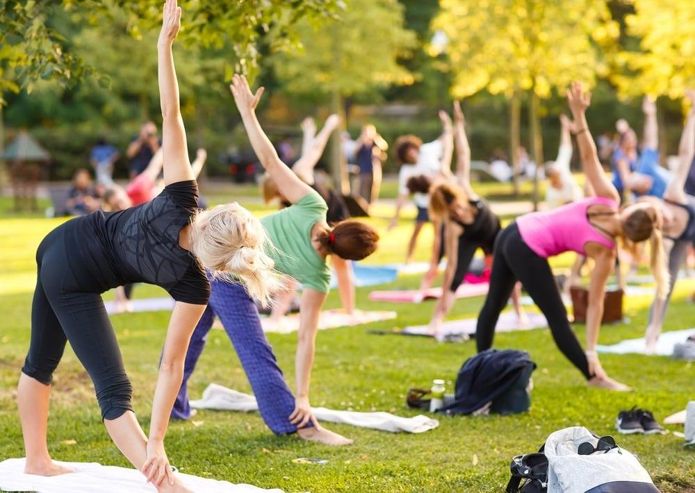 Outdoor yoga class with diverse participants stretching on mats in the park.