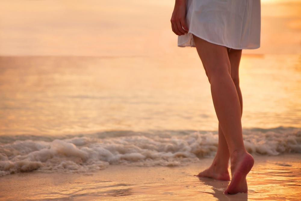 Walking barefoot by the waves at sunset on a serene beach.