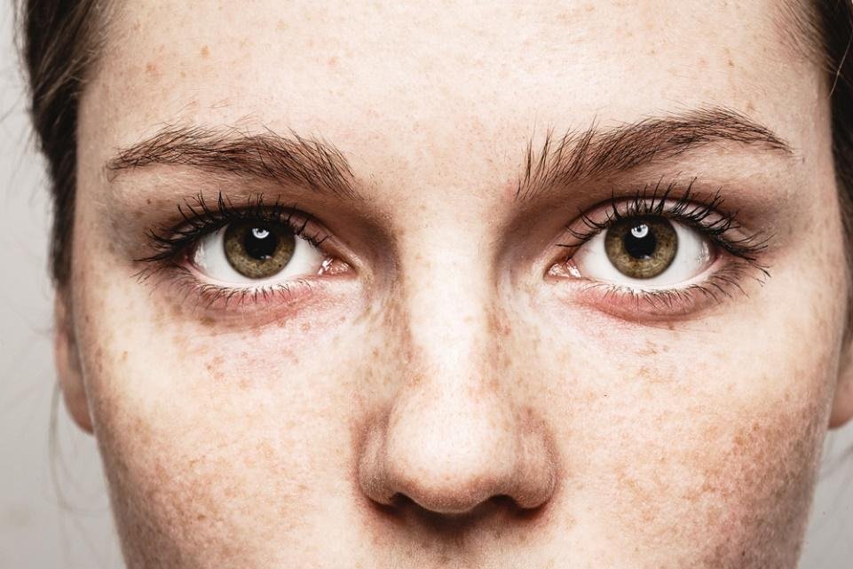 Freckled woman with captivating green eyes in a close-up portrait.