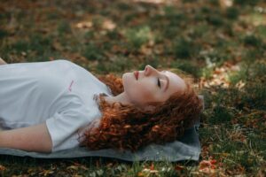 Relaxed woman lounging on grass in a serene forest setting.