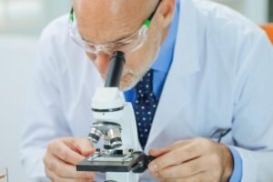 Scientist examining a specimen closely under a microscope in a laboratory setting.