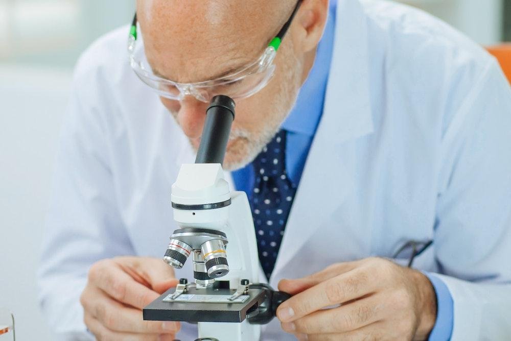 Scientist examining a specimen closely under a microscope in a laboratory setting.