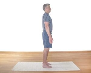 Man practicing standing yoga pose on a mat in a spacious room.