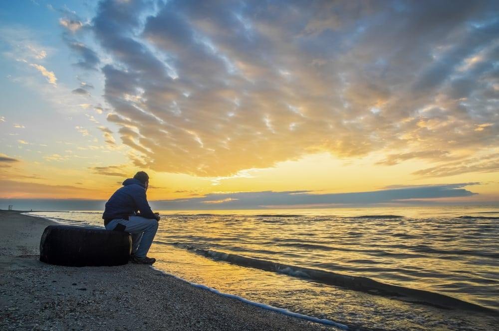Person enjoying a serene sunset at the beach, reflecting on the calm water.