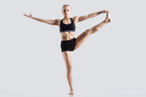 Graceful female dancer in a strong yoga pose against a light background.