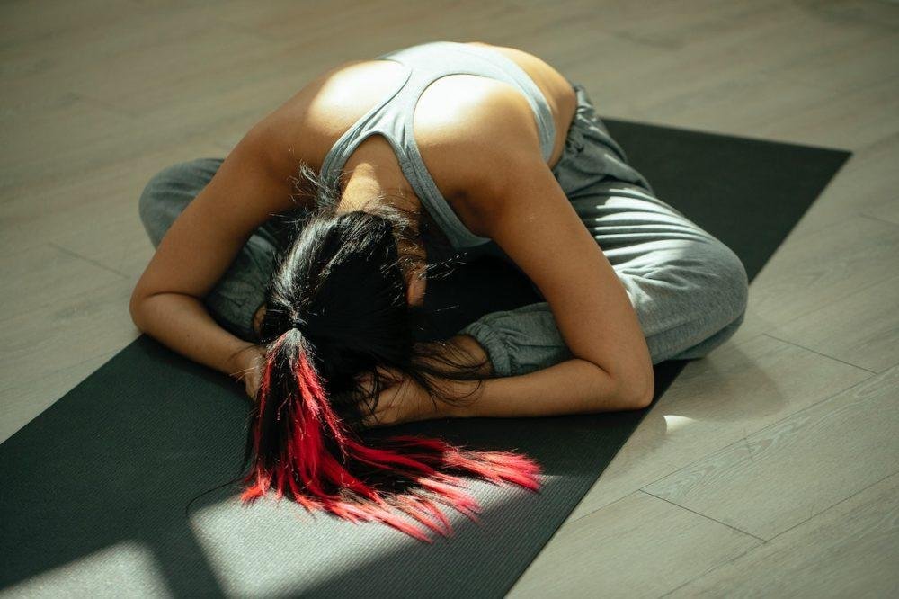 Yoga stretching pose with dark hair and red highlights on a mat.