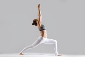 Woman practicing yoga in warrior pose with white leggings.