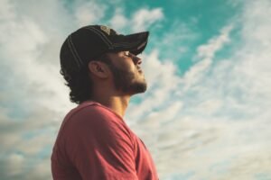 Man in black cap gazing thoughtfully at the cloudy sky.