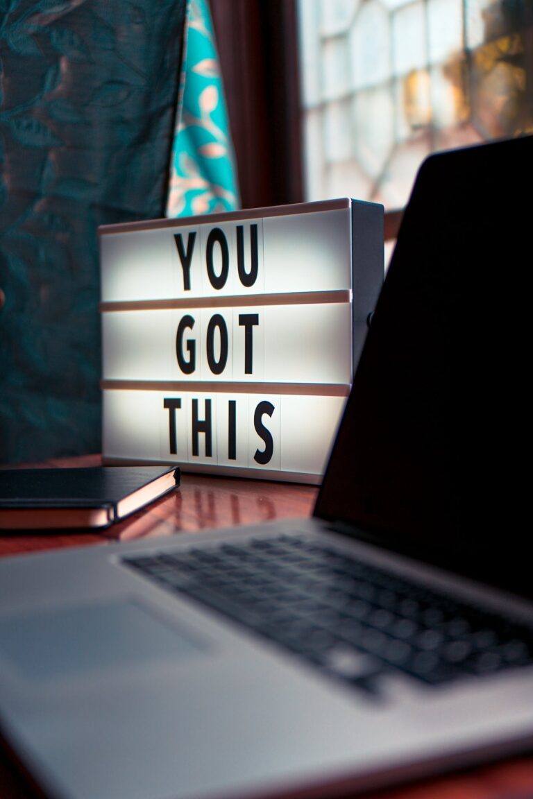 Illuminated motivational lightbox reading You Got This beside a laptop.
