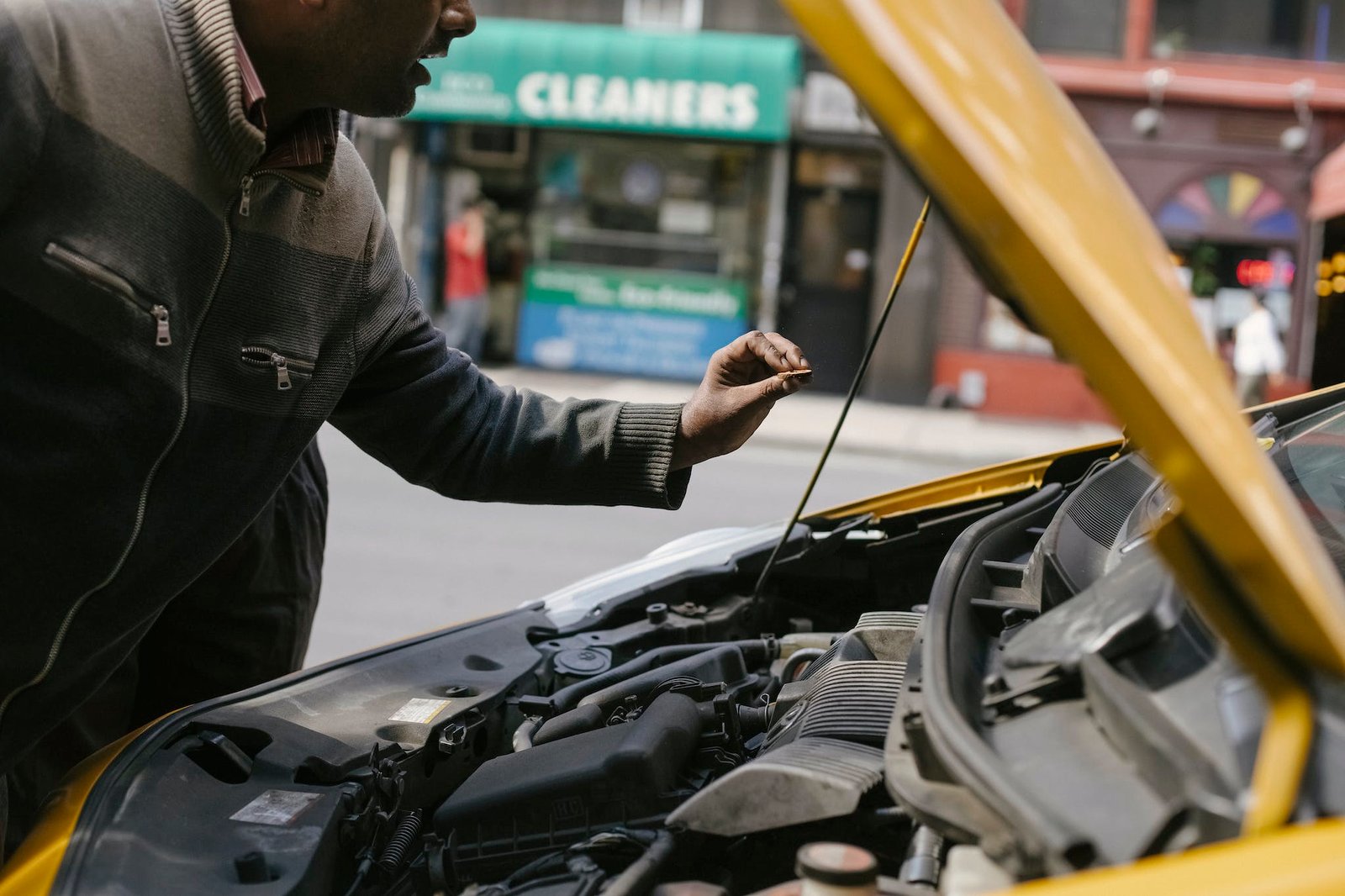 Mechanic inspecting a car engine under the hood in a city setting.