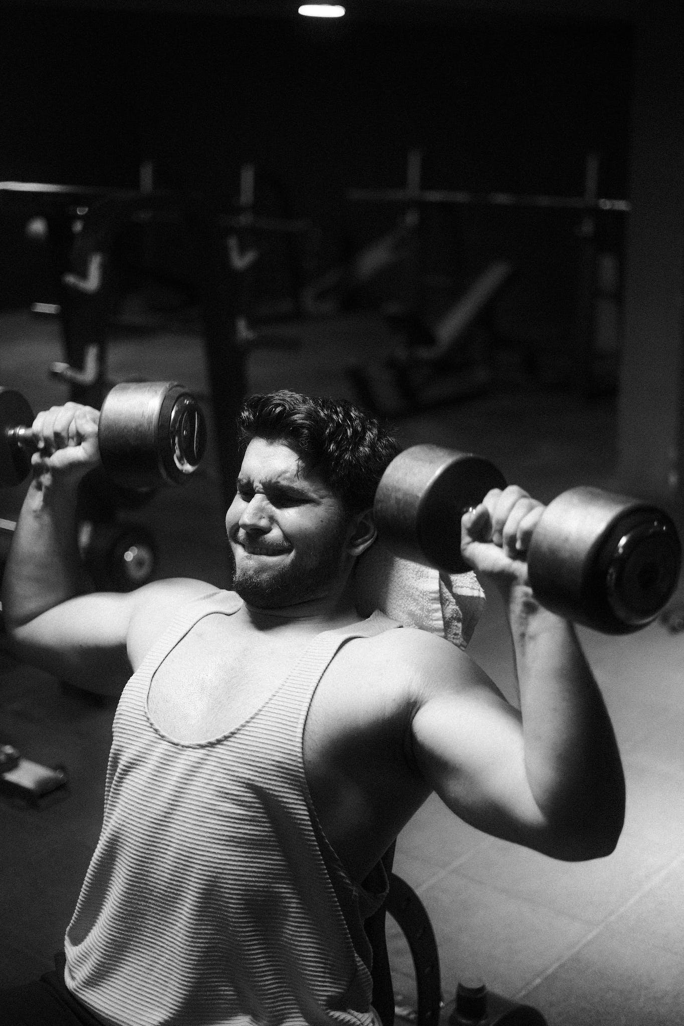Weightlifter exercising with dumbbells in a black and white gym setting.