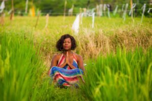 Woman meditating peacefully in a green field, surrounded by nature’s tranquility.