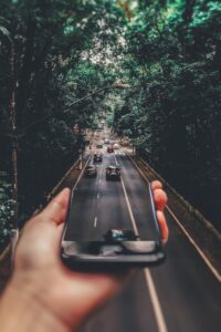 Innovative forced perspective photo of a smartphone above a busy tree-lined road.